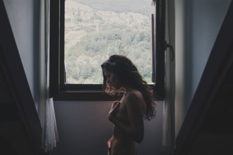 Side view of naked woman standing by window at home