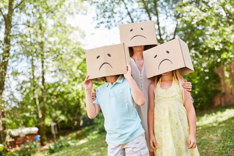 Woman with children wearing smiley face cardboard box on grassy field