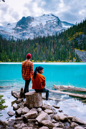Rear view of couple by lake against mountains and sky