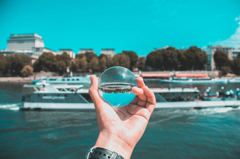 Cropped hand holding crystal ball against river