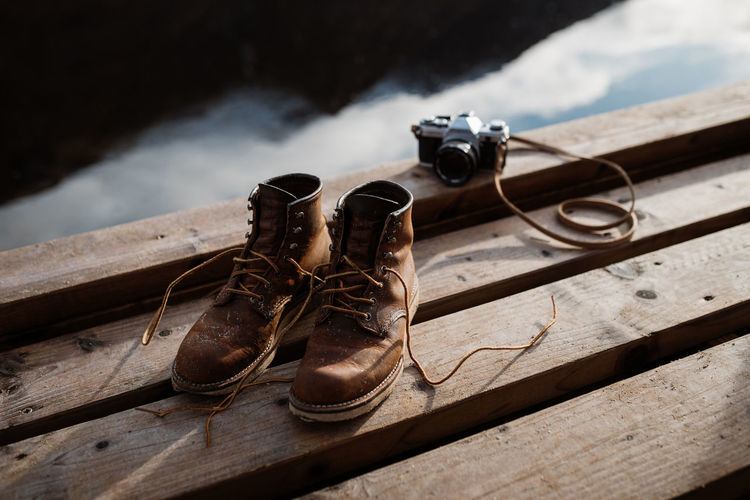 High angle of pair of dirty trekking boots placed on wooden quay near retro photo camera in scottish highlands