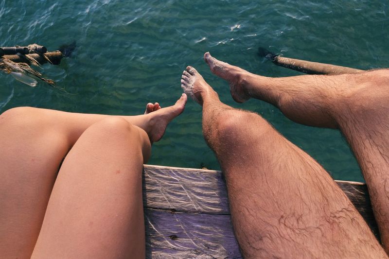 Low section of couple sitting against rippled water