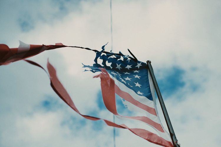Low angle view of abandoned american flag waving against cloudy sky