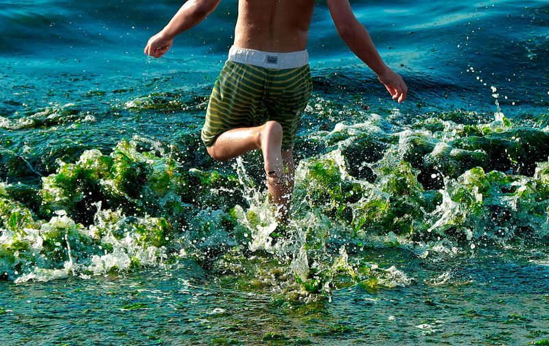 Low section of shirtless man running in sea