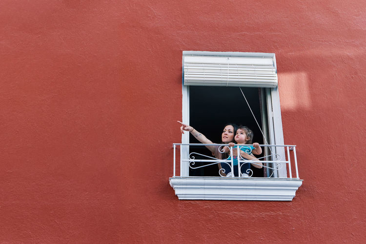 Woman clapping in the window of her house with her daughter on a red background