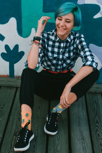 Full length of smiling woman sitting on wood against wall