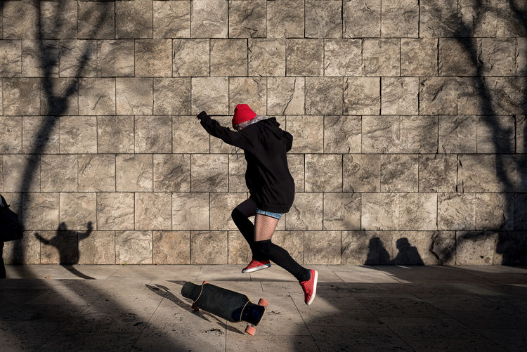 Full length of man skateboarding on footpath against wall