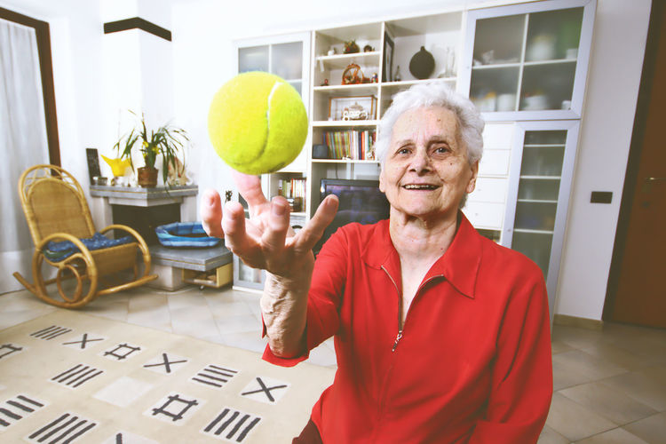 Portrait of happy senior woman catching ball at home