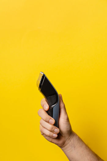 Close-up of hand holding smart phone against yellow background