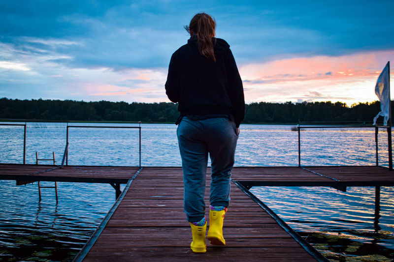 Rear view of woman standing on pier over lake against sky