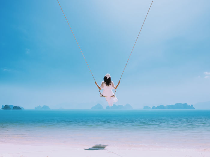 Woman holding umbrella in sea against sky