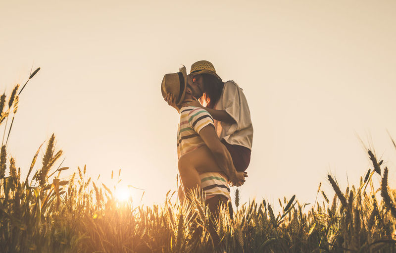 Couple kissing while standing against sky during sunset