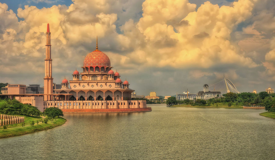 View of temple building by river against cloudy sky