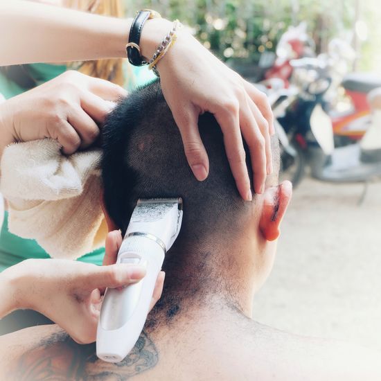 Cropped hands of person shaving man head