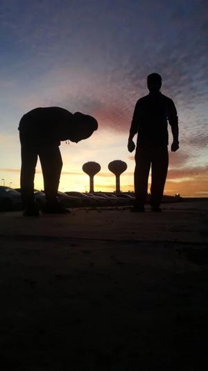 Silhouette men standing on shore against sky during sunset