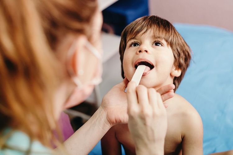From above of little boy with mouth opened being examined by female doctor in clinic