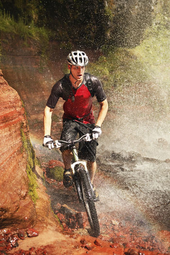 Wet young man cycling by waterfall