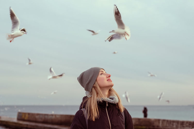 side view of woman feeding seagulls at beach against sky