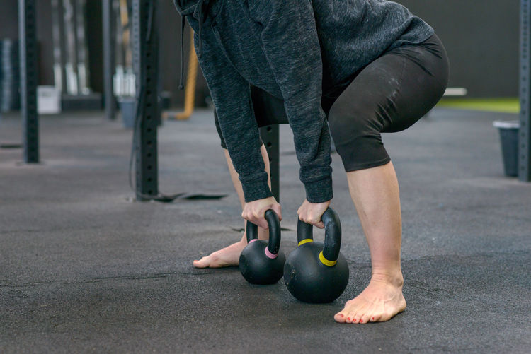 Low section of female athlete exercising with kettlebells in gym