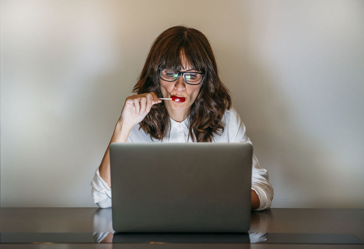 Woman with glasses works with computer and eats a candy