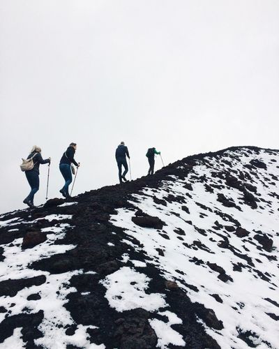 Friends climbing snowcapped mountain against clear sky