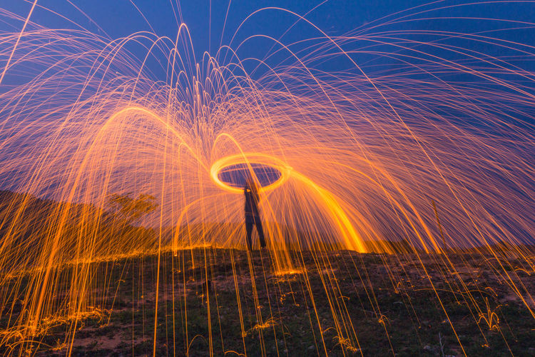 Man spinning illuminated wire wool at night