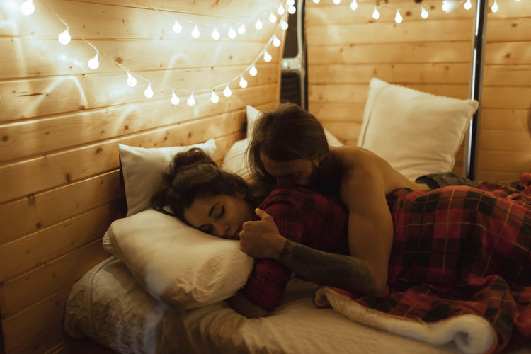 Man kissing girlfriend lying on bed in camper van