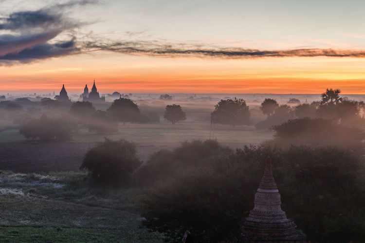 Temples and trees on landscape against sky during sunset
