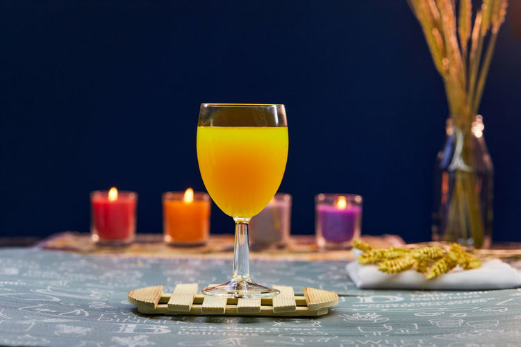 Glass of orange juice on wooden plate with candlelight on table