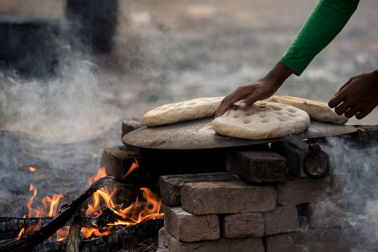Close-up of hand roasting flatbreads on fire