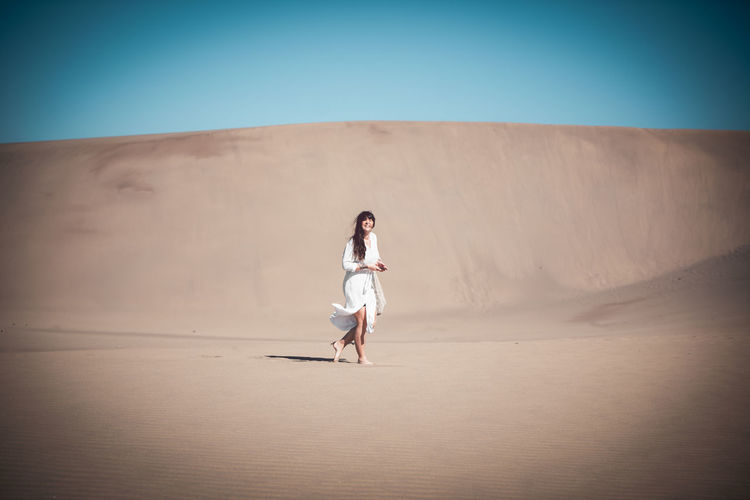 Side view of woman walking on sand dune at desert against clear sky during sunny day