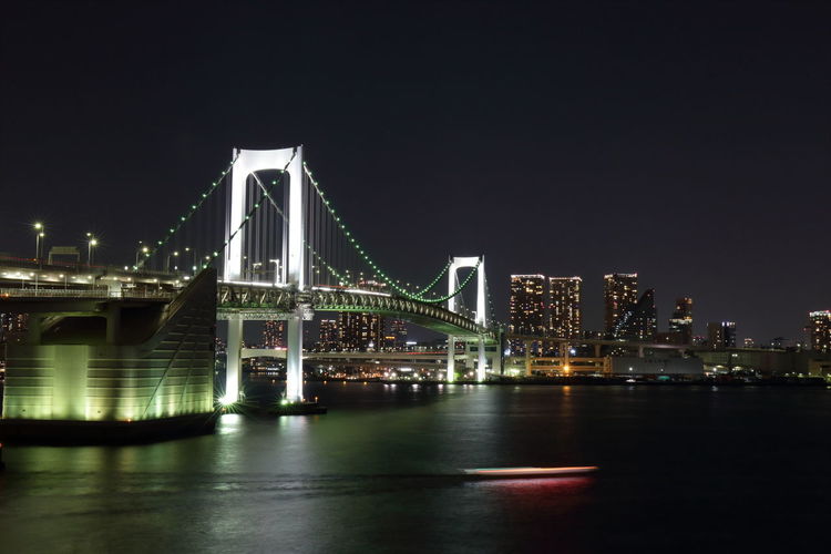 Illuminated rainbow bridge over tokyo bay in city at night
