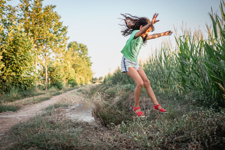 Girl wirh long dark hair jumping over pit with arms up in corn field