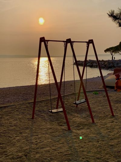Empty swing at beach against sky during sunset