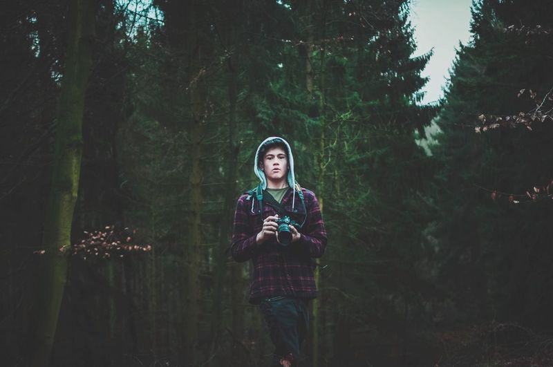 Portrait of young man with camera standing in forest