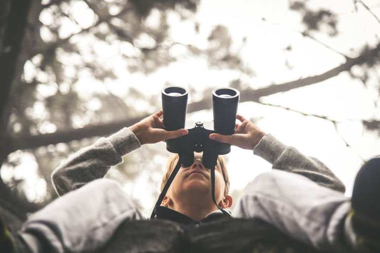 Low angle view of boy looking through binoculars at forest