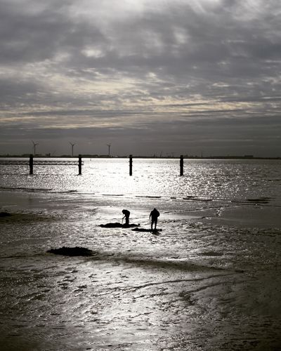 Silhouette people standing on beach against sky during sunset
