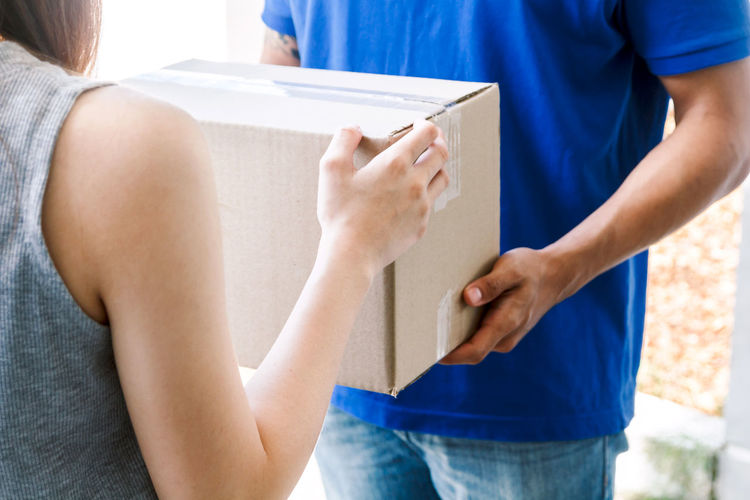 Midsection of woman receiving cardboard box from delivery person outdoors