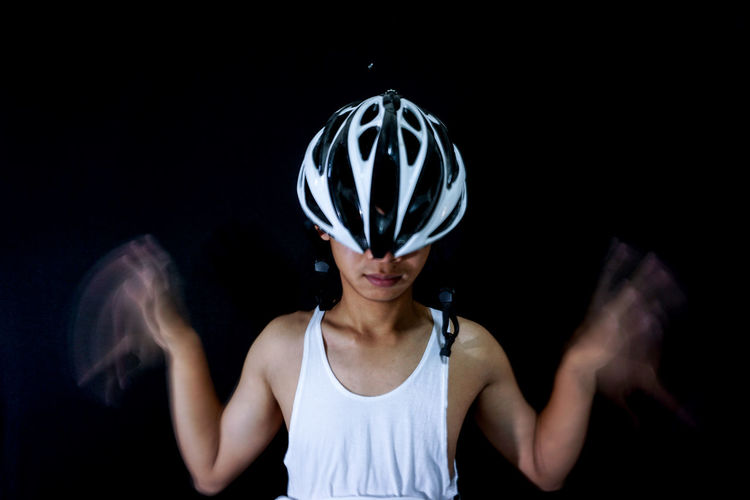 Close-up of man with blurred hands wearing bicycle helmet against black background