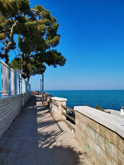 Footpath by sea against clear blue sky