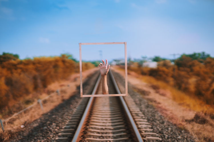 Digital composite image of hand over railroad track against sky