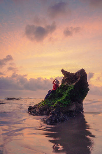 Woman on rock amidst sea during sunset