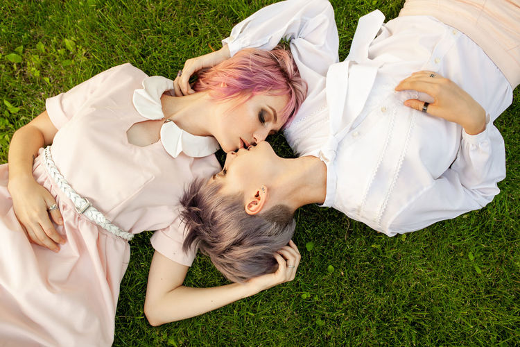 Directly above shot of young lesbians kissing while lying on grassy field