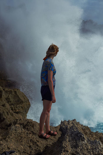 Woman standing on rock looking at mountain against sky