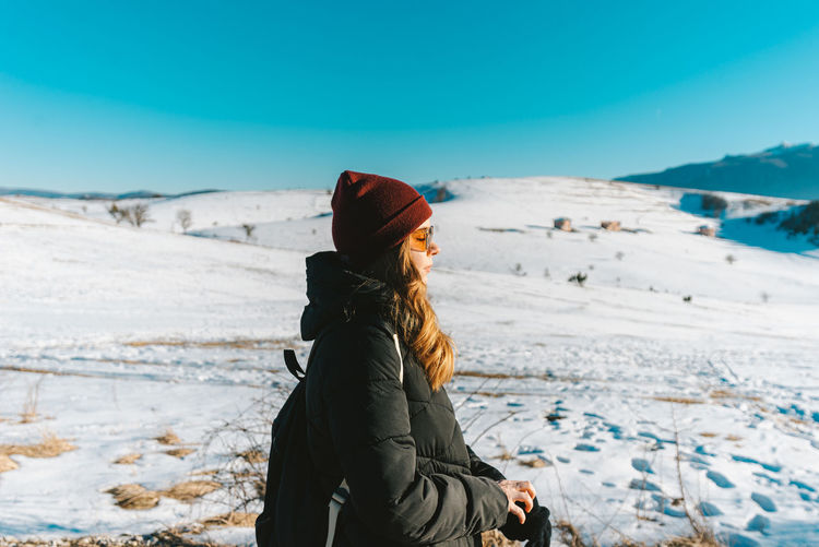 Side view of young woman standing on snow covered land