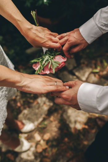 Newlyweds with their hands clasped, with their wedding rings and bouquet of roses. 