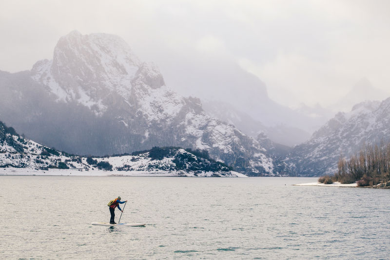 Tourist floating on sup between water surface and picturesque view of hills in snow in riaño, león, spain