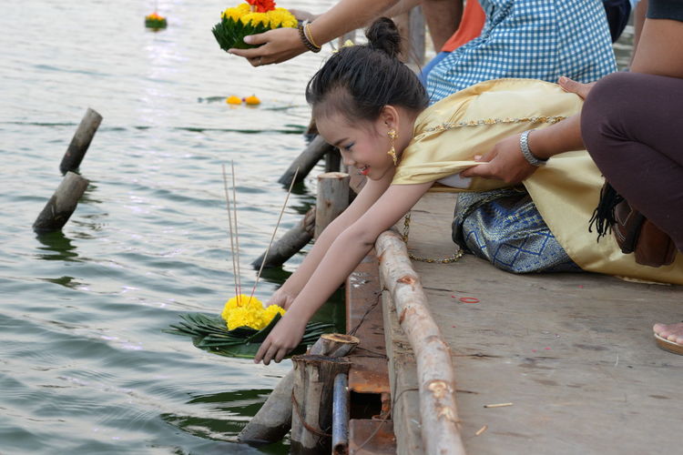 Girl with mother worshipping flowers and incense over lake