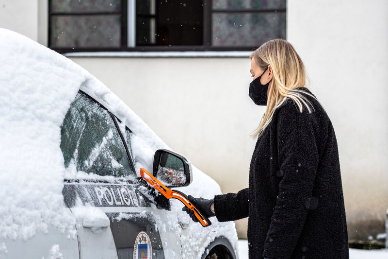 Blond woman in face mask with a squeegee cleans snow from a police car