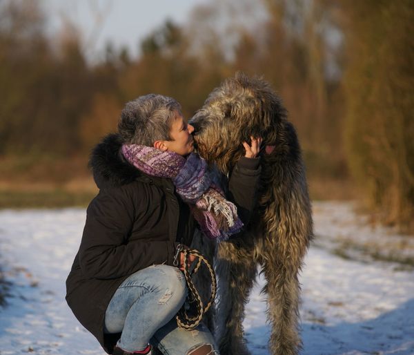 Woman kissing dog on snow covered field